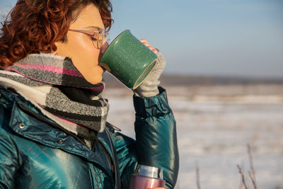 Rear view of woman drinking water while standing at beach