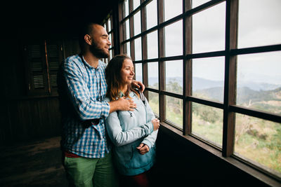 Happy friends standing against window