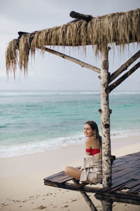 Woman sitting on beach by sea against sky