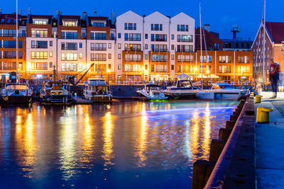 Boats moored in illuminated canal by buildings in city at night