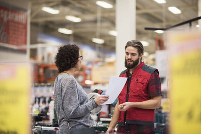 Salesman discussing with female customer holding document in hardware store