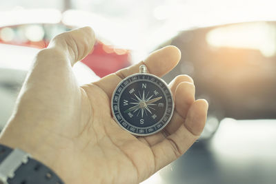 Cropped hand holding compass against cars