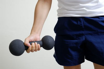 Midsection of man holding dumbbell while standing against wall