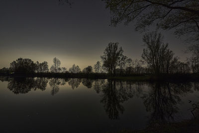 Reflection of silhouette trees in lake against sky