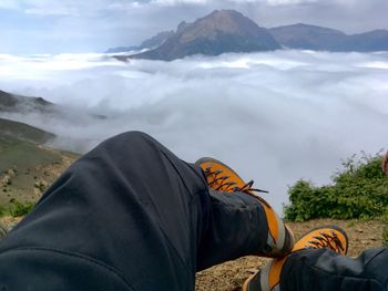 Low section of man sitting on mountain against cloudy sky