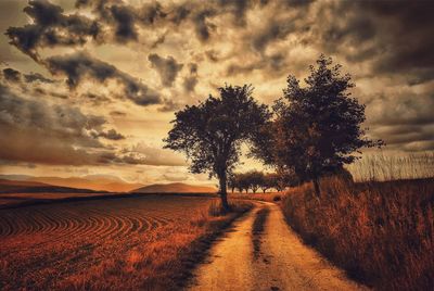 Road passing through field against cloudy sky