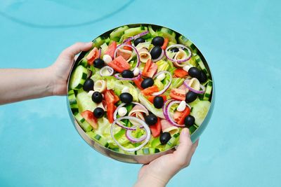 Cropped image of person holding plate full to salad by poolside