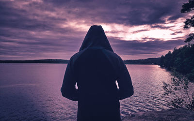 Rear view of man standing by lake during sunset