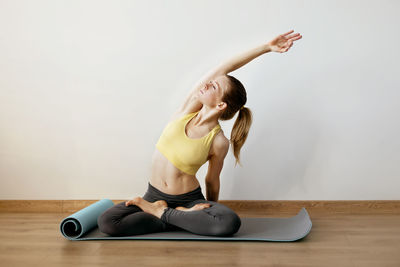 Full length of young woman sitting on floor against wall