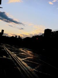 Road by silhouette buildings against sky during sunset