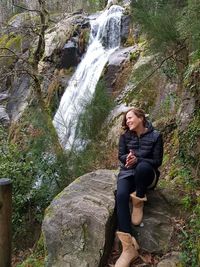 Portrait of young woman sitting on rock against trees