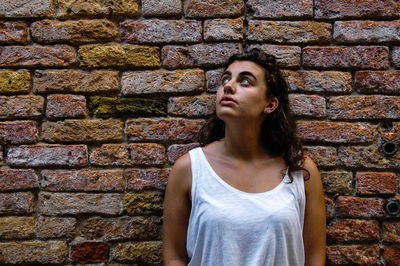 Portrait of beautiful young woman standing against brick wall