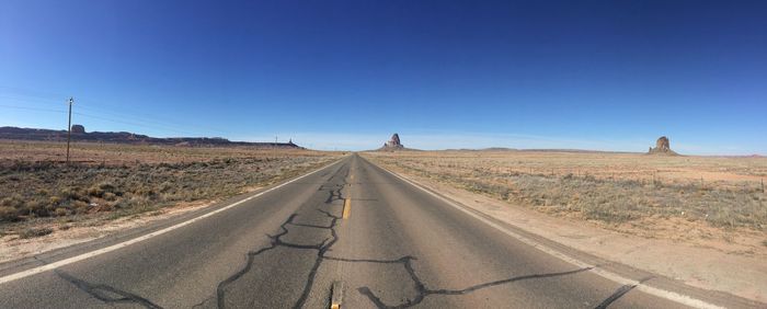 Road amidst desert against clear blue sky