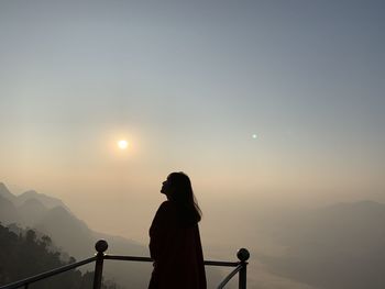 Silhouette person standing by railing against sky during sunset