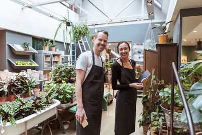 Portrait of male and female partners with digital tablet by plants at store