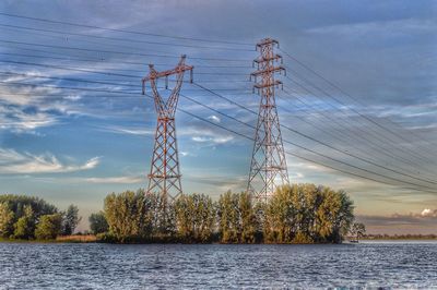 Electricity pylon by trees against sky