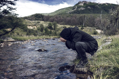 Thirsty man drinking water from stream at forest