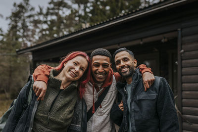 Portrait of cheerful multiracial friends standing in front of cabin during vacation