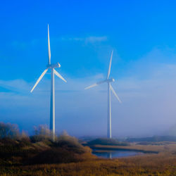 Wind turbines on field against blue sky