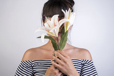 Woman hiding face by flowers against white background