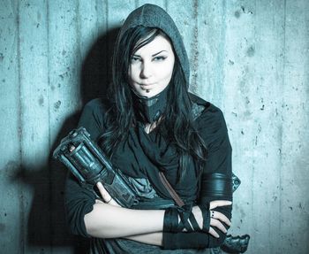 Portrait of smiling young beautiful woman holding gun while standing against wall