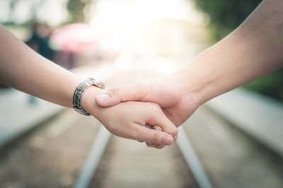 Cropped image of couple holding hands above railroad tracks