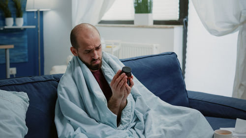 Side view of young man using mobile phone while lying on bed at home