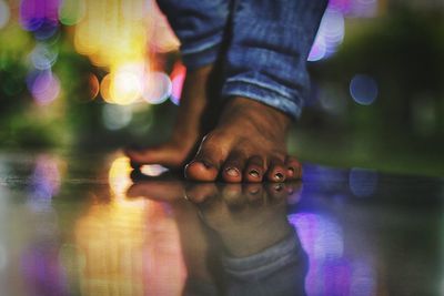 Low section of people standing on glass floor with defocused lights reflection