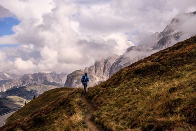 Rear view of man hiking on mountain against cloudy sky