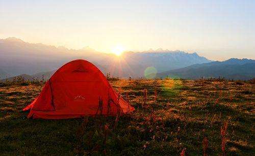 Tent in field against sky during sunset