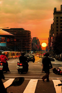 People on city street against sky during sunset