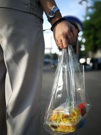 Midsection of man holding food in plastic bag on road