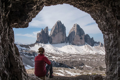 Rear view of man sitting on rock against sky