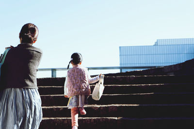 Rear view of mother with daughter walking on staircase