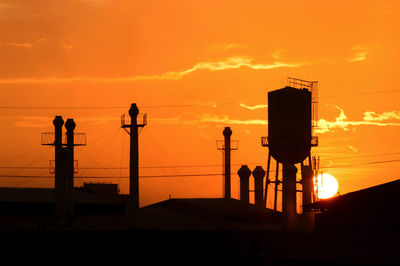 Silhouette industrial buildings against orange sky