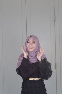 Portrait of a smiling young woman standing against wall