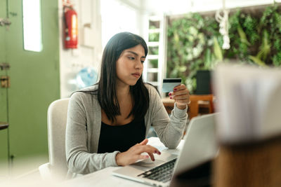 Female making purchase with plastic card for order during online shopping via laptop