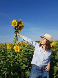 Beautiful woman holding sunflower on field against sky