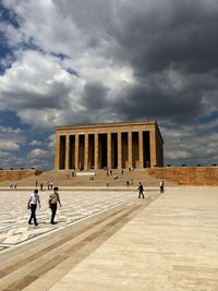 People in front of historical building against cloudy sky