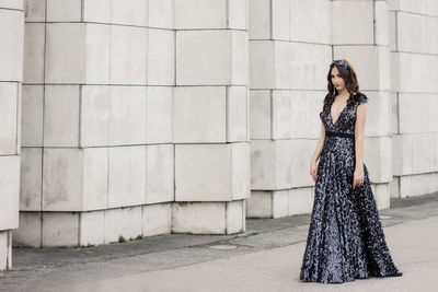 Portrait of beautiful woman wearing evening gown while standing by wall