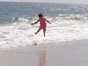 Rear view of girl jumping in water at beach