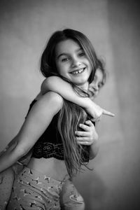 Portrait of smiling girl piggybacking sister against wall at home