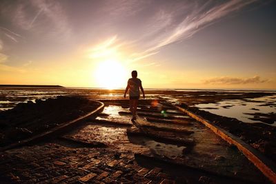 Rear view of woman walking at beach during sunset