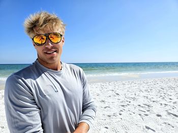 Portrait of young man wearing sunglasses standing at beach