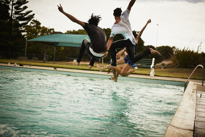 People jumping in swimming pool against sky