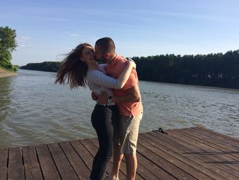 Man kissing woman while standing on jetty at lake
