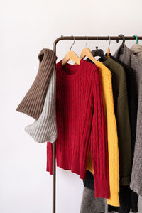 Row of different colorful knitted sweaters hang on hangers, white background