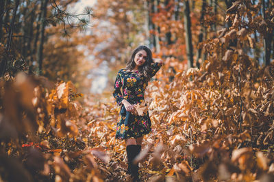 Young woman standing by tree in forest during autumn