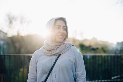 Back lit of smiling young muslim woman wearing hijab against sky