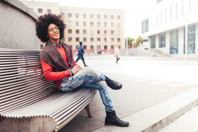 Thoughtful young man smiling while sitting on bench in city